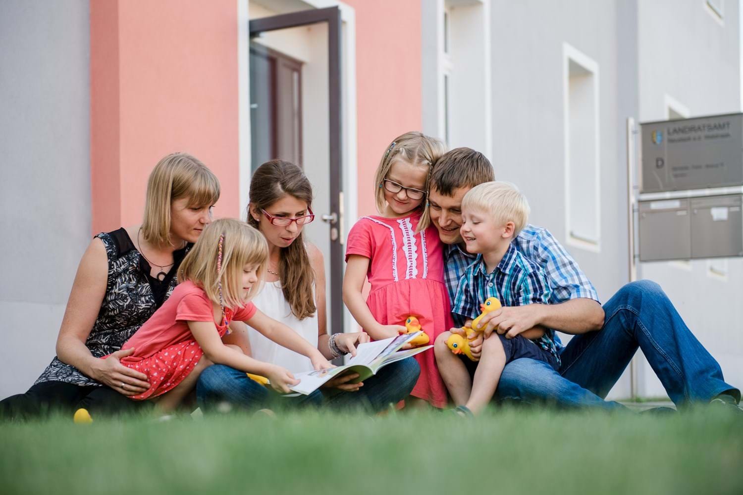 Eine Familie befindet sich eine Wiese und schaut zusammen ein Buch an.