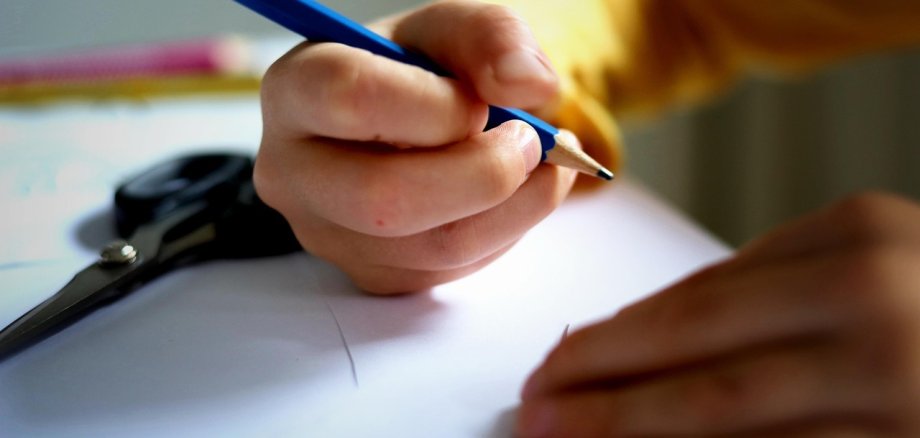 Ein Kind hält einen blauen Bleistift in der Hand und schreibt oder zeichnet auf ein Blatt Papier.
