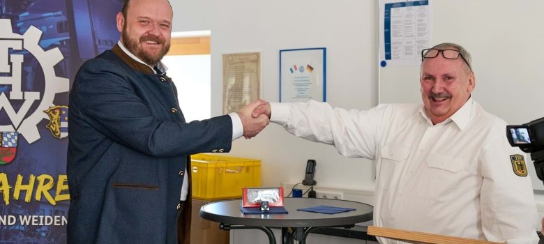 Landrat Andreas Meier übergibt Michael Braun einen kleinen THW-Kipper im Miniaturmaßstab 1:87 mit funktionierendem Blaulicht.