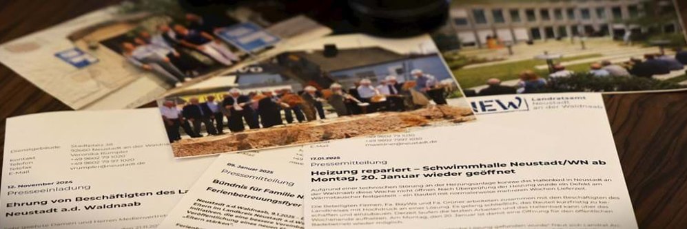 Nahaufnahme verschiedener Pressemitteilungen und Einladungsschreiben des Landratsamts Neustadt an der Waldnaab, teilweise überlagert von Farbfotos mit Szenen offizieller Veranstaltungen und Gebäuden.