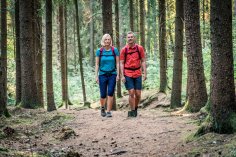 Ein Paar wandert auf einem schattigen Waldweg durch einen dichten Nadelwald.