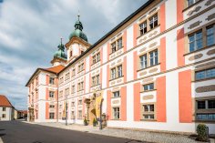 Barockes Kloster und Klosterdorf Speinshart
© Oberpfälzer Wald, Fotograf Thomas Kujat Barockes Klostergebäude in Speinshart mit auffälliger Fassade in Weiß und Ockerrot sowie grünen Zwiebeltürmen. Vor dem Eingang wehen Fahnen, die Architektur spiegelt die historische Bedeutung des Klosterdorfs wider.