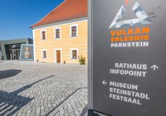 Vulkanerlebnis Parkstein
© Oberpfälzer Wald, Fotograf Thomas Kujat Eingangsbereich des Vulkanerlebnis Parkstein mit einem historischen gelben Gebäude und einem modernen Anbau aus dunklem Metall.