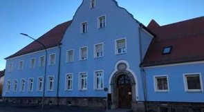 Dienstgebäude Vohenstrauß: Altbau mit blau gestrichener Fassade und rotem Satteldach, das Gebäude hat eine historische Architektur mit einem geschwungenen Giebel