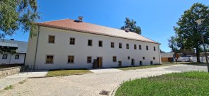 Dienstgebäude Vohenstrauß: Großes historisches Gebäude mit weißer Fassade und rotem Ziegeldach. Vor dem Gebäude befindet sich ein gepflasterter Platz mit Grünflächen.