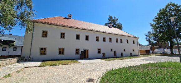 Dienstgebäude Vohenstrauß: Großes historisches Gebäude mit weißer Fassade und rotem Ziegeldach. Vor dem Gebäude befindet sich ein gepflasterter Platz mit Grünflächen.