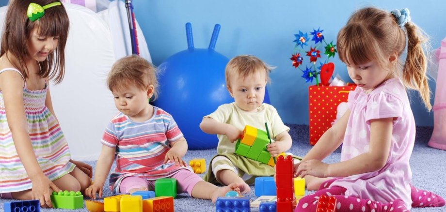 Vier Kinder in unterschiedlichem Alter spielen mit Bauklötzen in einem Spielezimmer zusammen.